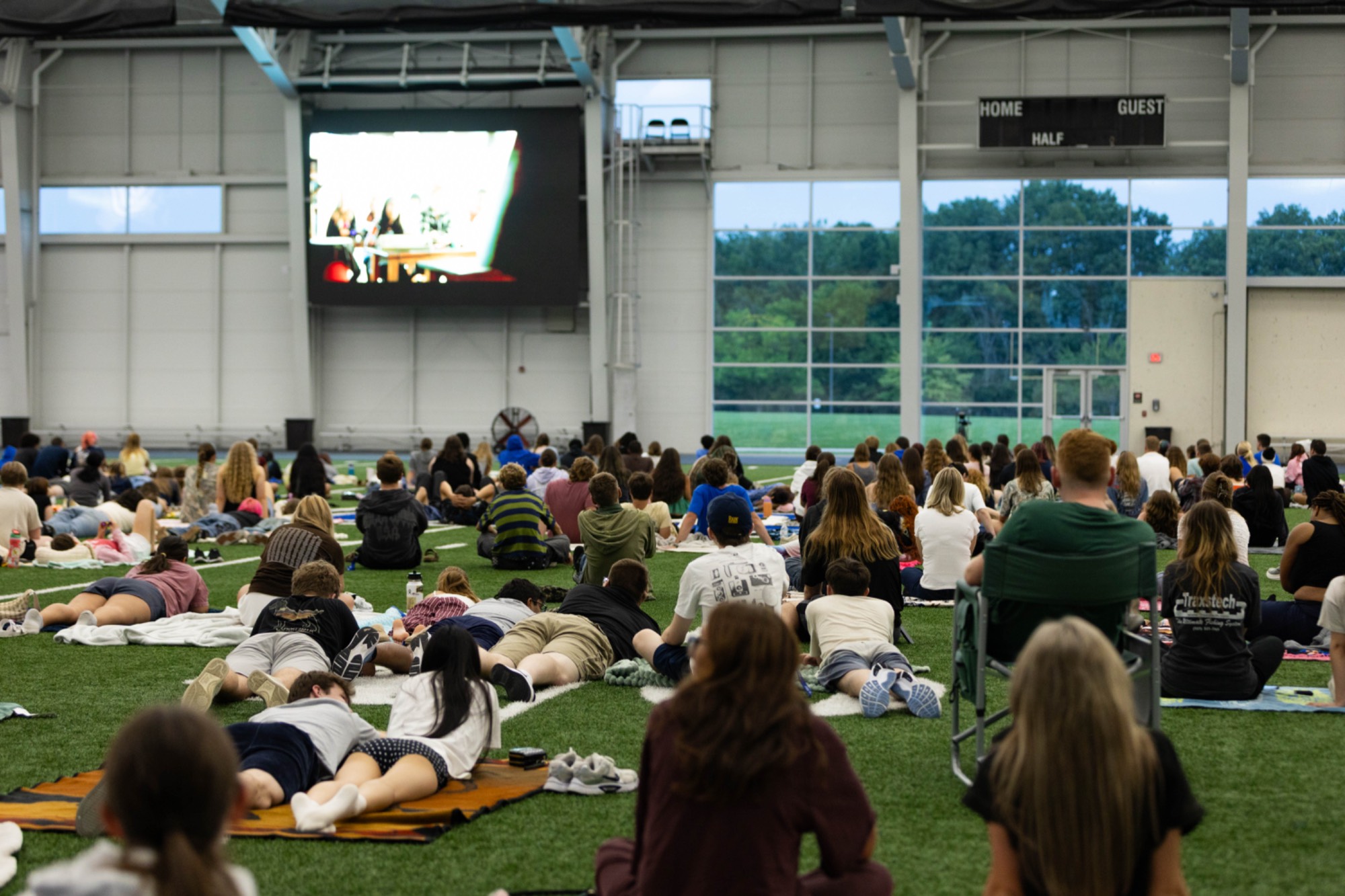 Students sit on the field at the Kelly, watching a movie on the big screen